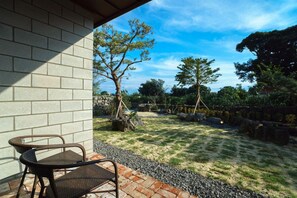 A patio with a brick wall, a wicker chair, and a garden with trees and a gravel path. - Misoga Pension (Seogwipo)