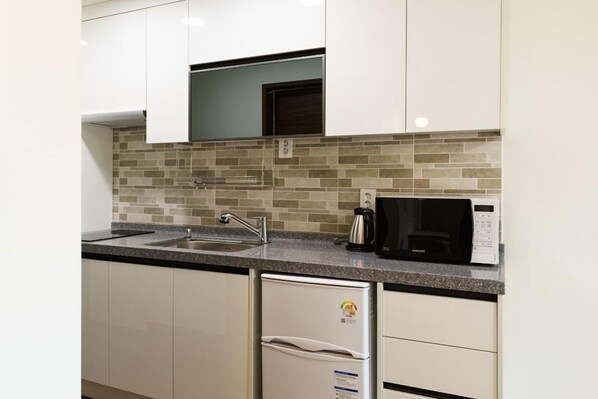 Una cocina moderna con gabinetes blancos, encimera de granito, microondas integrado y refrigerador de acero inoxidable.