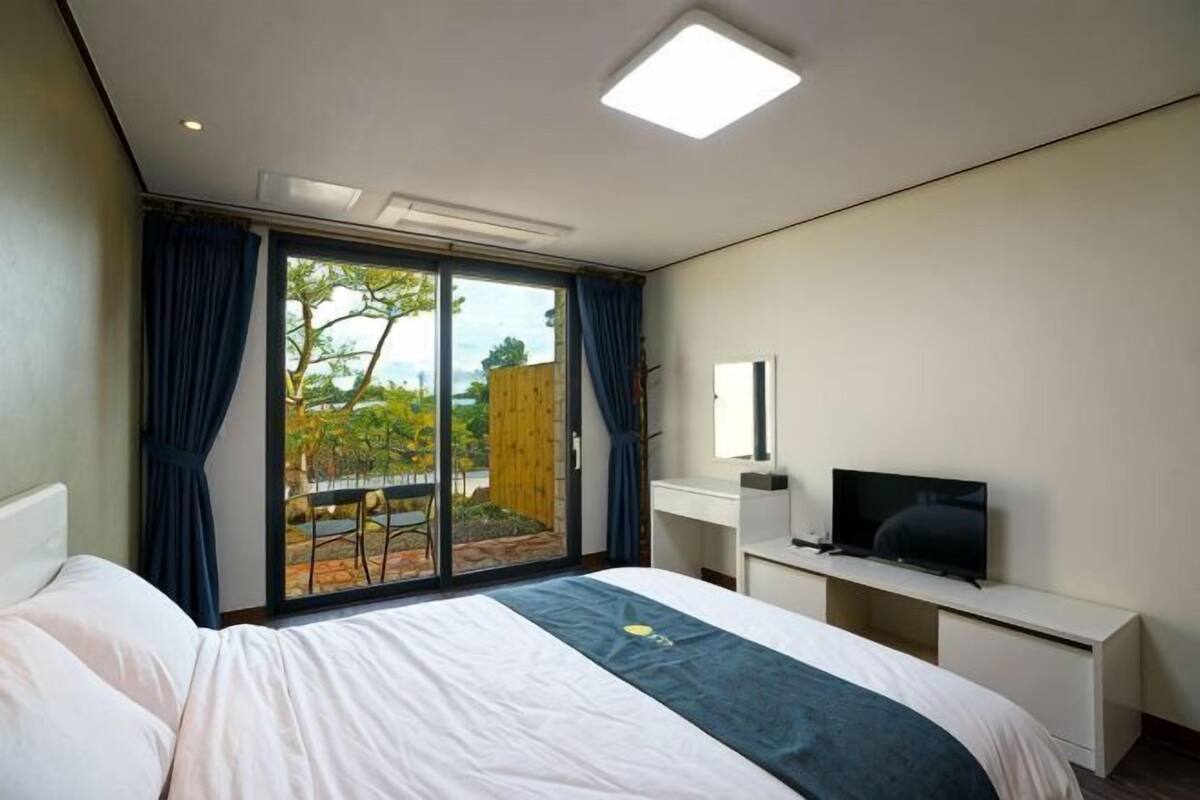 A bedroom with a bed, a TV, a desk, and a sliding glass door leading to an outdoor area.