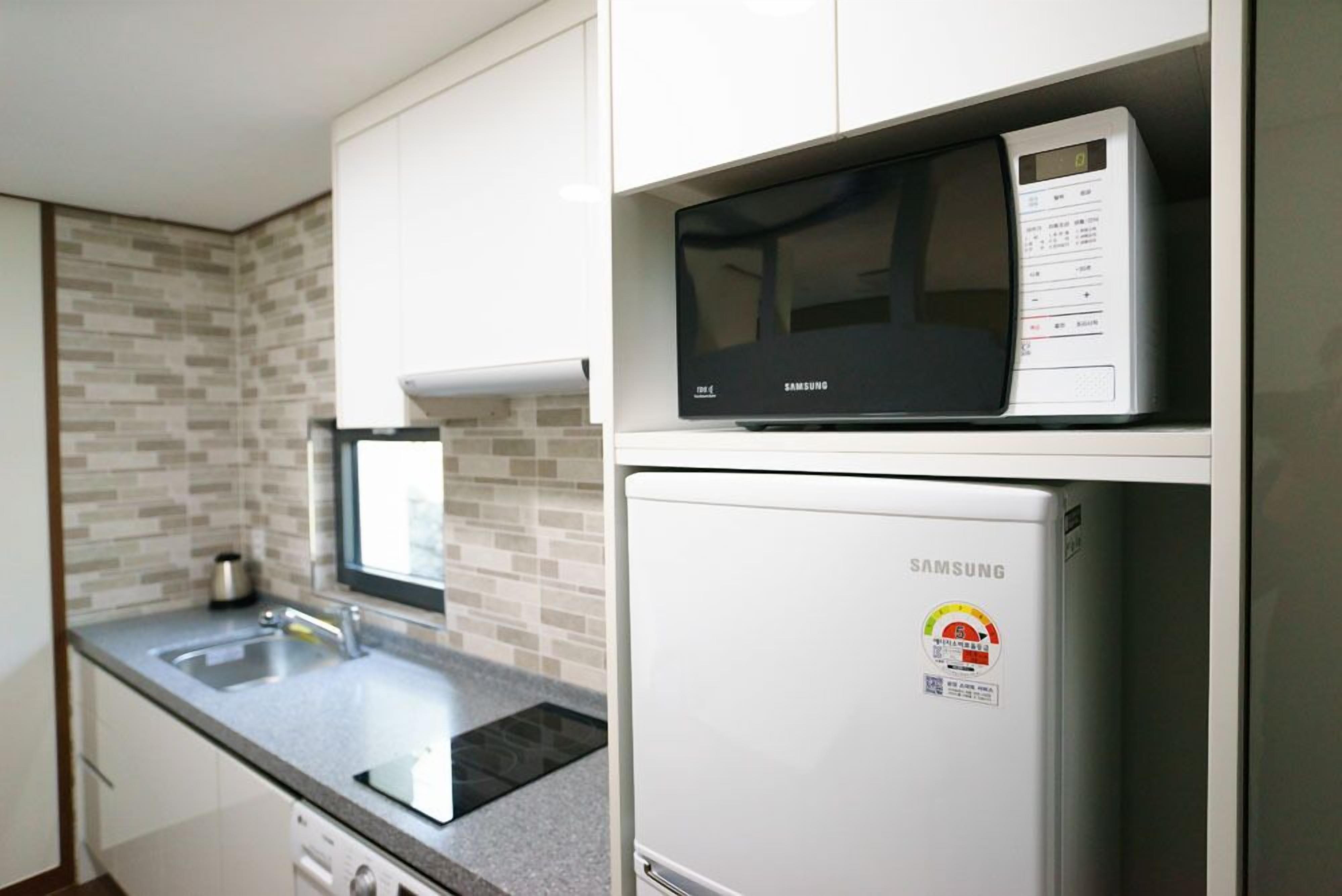 A compact kitchen with a microwave and a refrigerator, a sink, and a tiled backsplash.