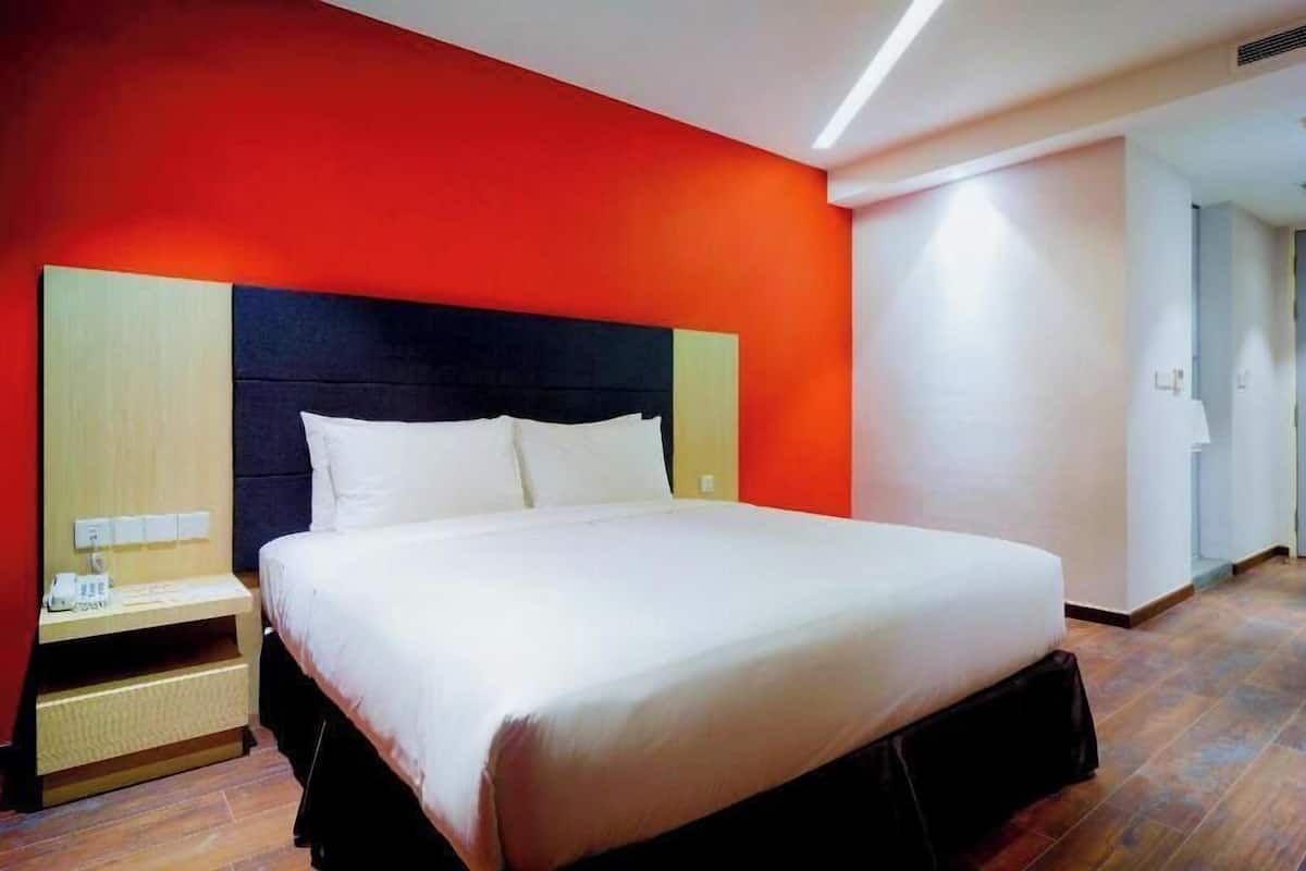A hotel room with a bed, a nightstand, and a red wall.