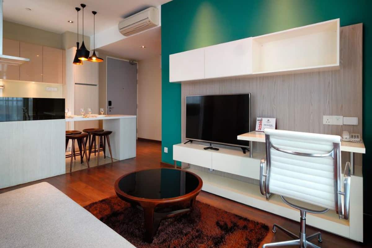 A modern living room with a kitchen area, a round coffee table, and a TV on a white cabinet.