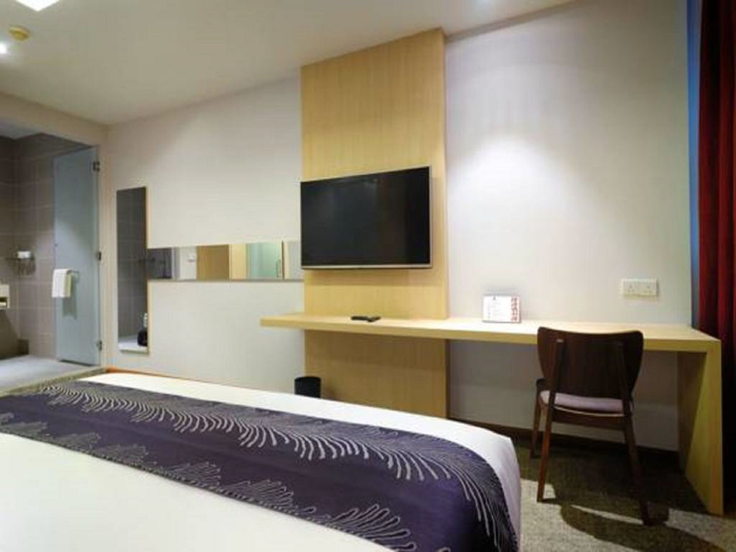 A hotel room with a bed, a desk, a chair, a TV, and a shower area.