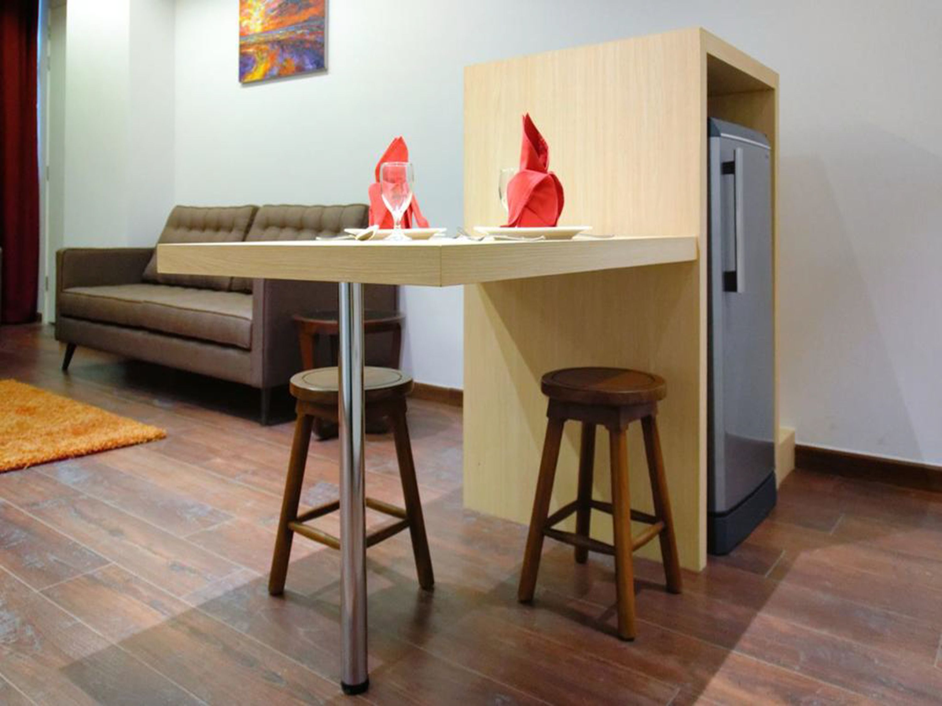 A compact living space with a small table and stools, a sofa, and a refrigerator.