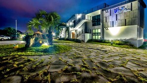 Un edificio moderno con entrada empedrada en piedra, palmeras y un letrero bien iluminado.