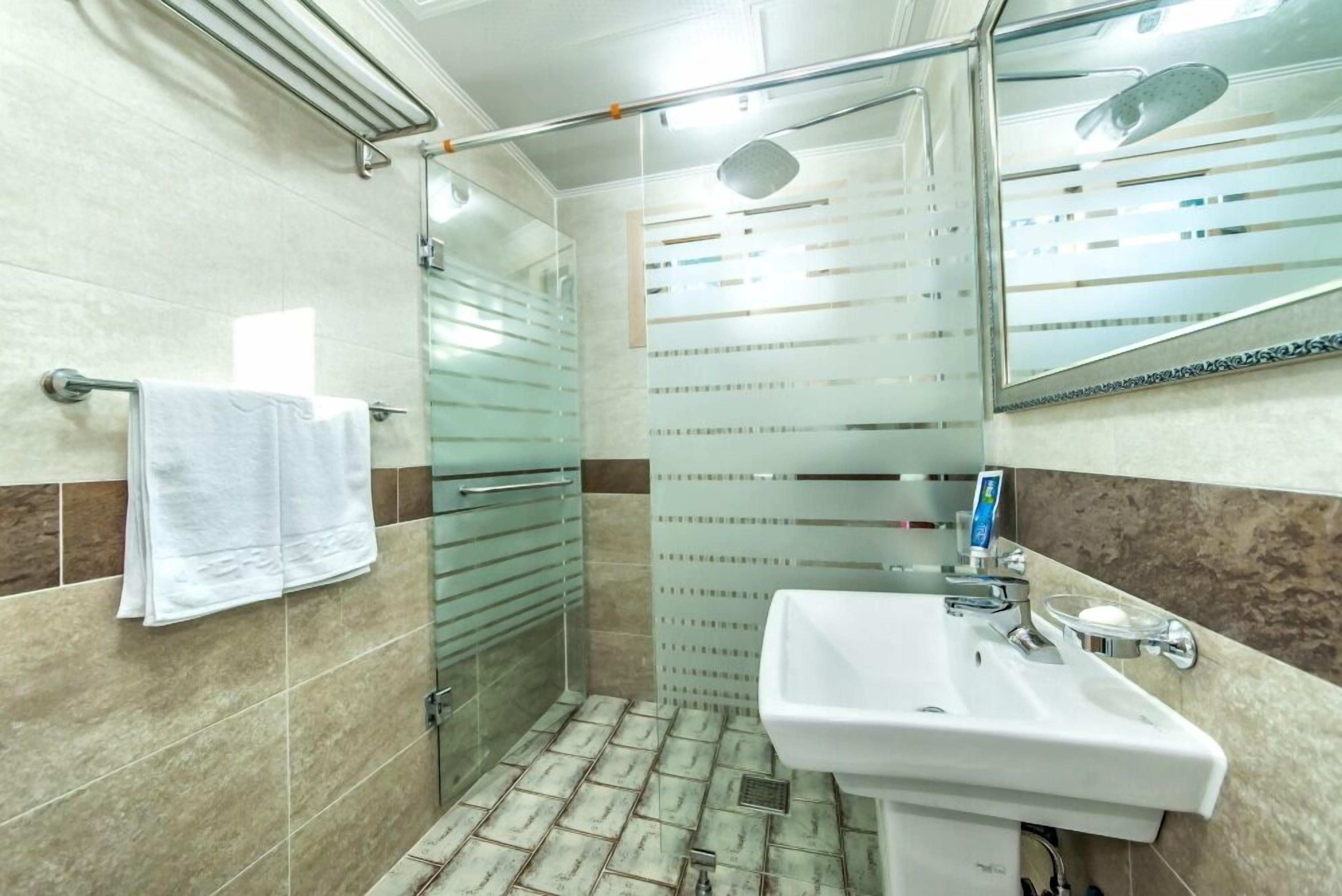 A bathroom with a glass shower enclosure, a white sink, and a towel rack.