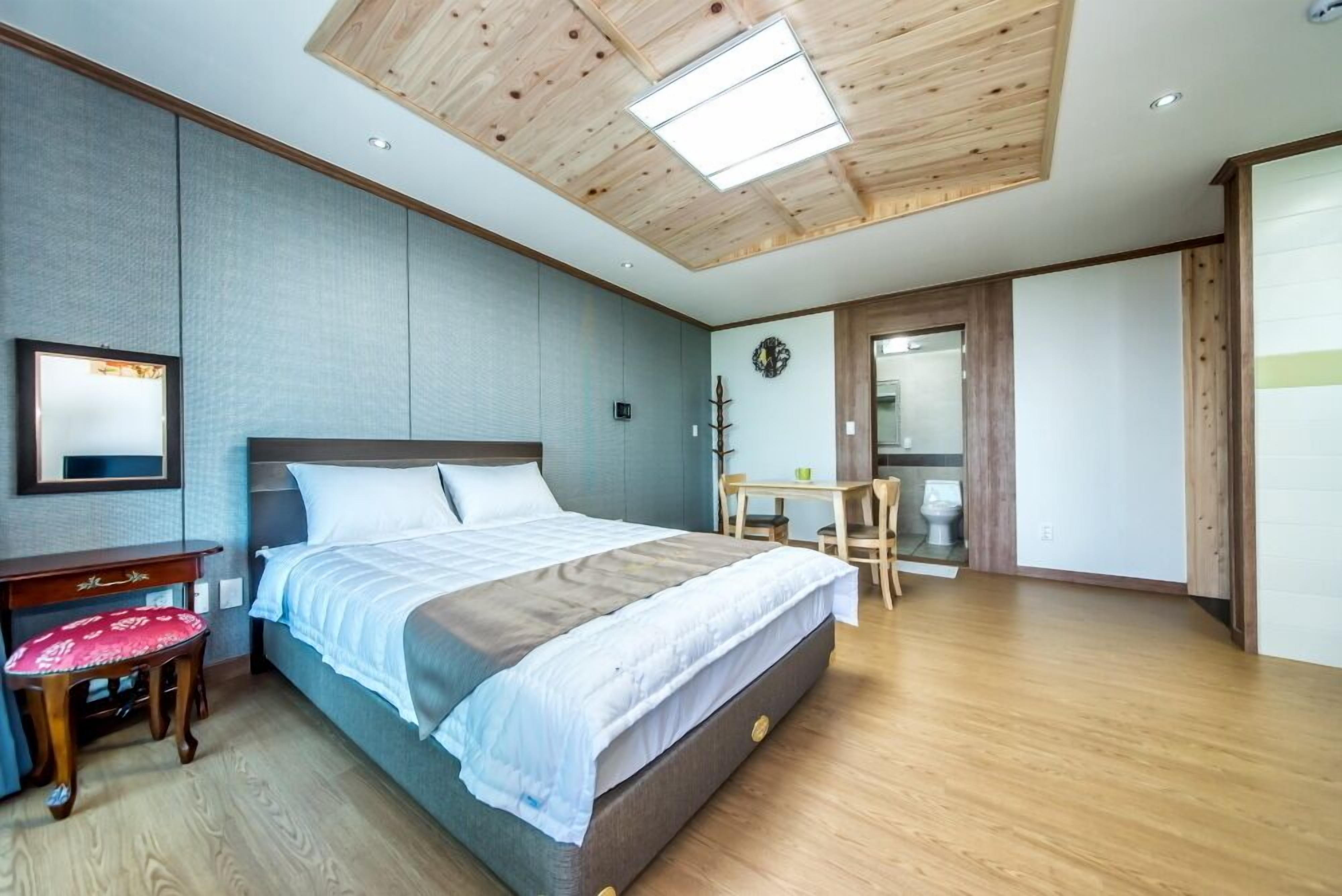 A bedroom with a wooden ceiling, a bed with white bedding, a small table with chairs, and a mirror on the wall.