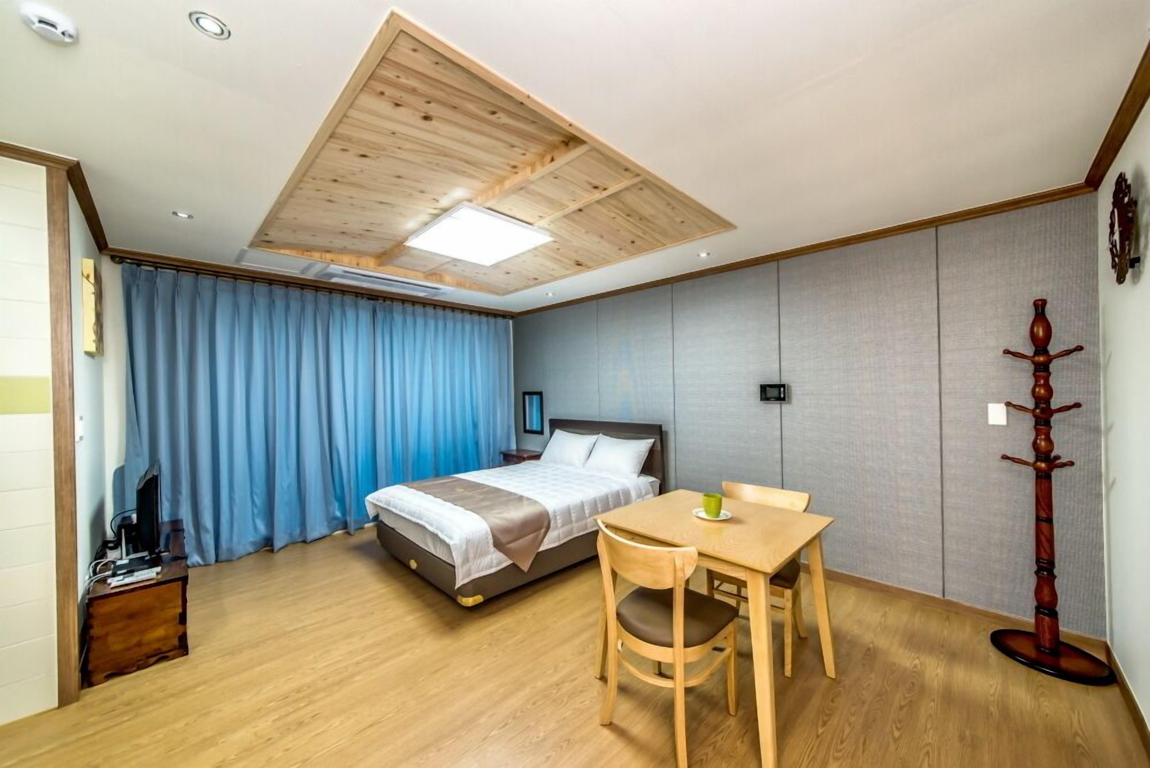 Quarto com cama, escrivaninha, cadeira, porta-casacos e teto com claraboias.