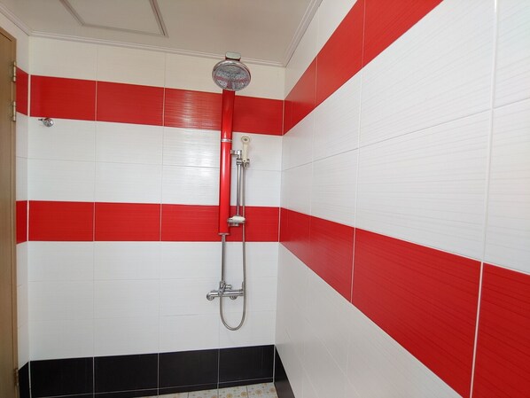 A bathroom with red and white tiled walls, a shower with a red hose, and a black tiled floor.