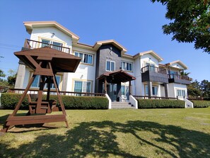 A large, multi-story house with a prominent front entrance, a balcony, and a well-maintained lawn.