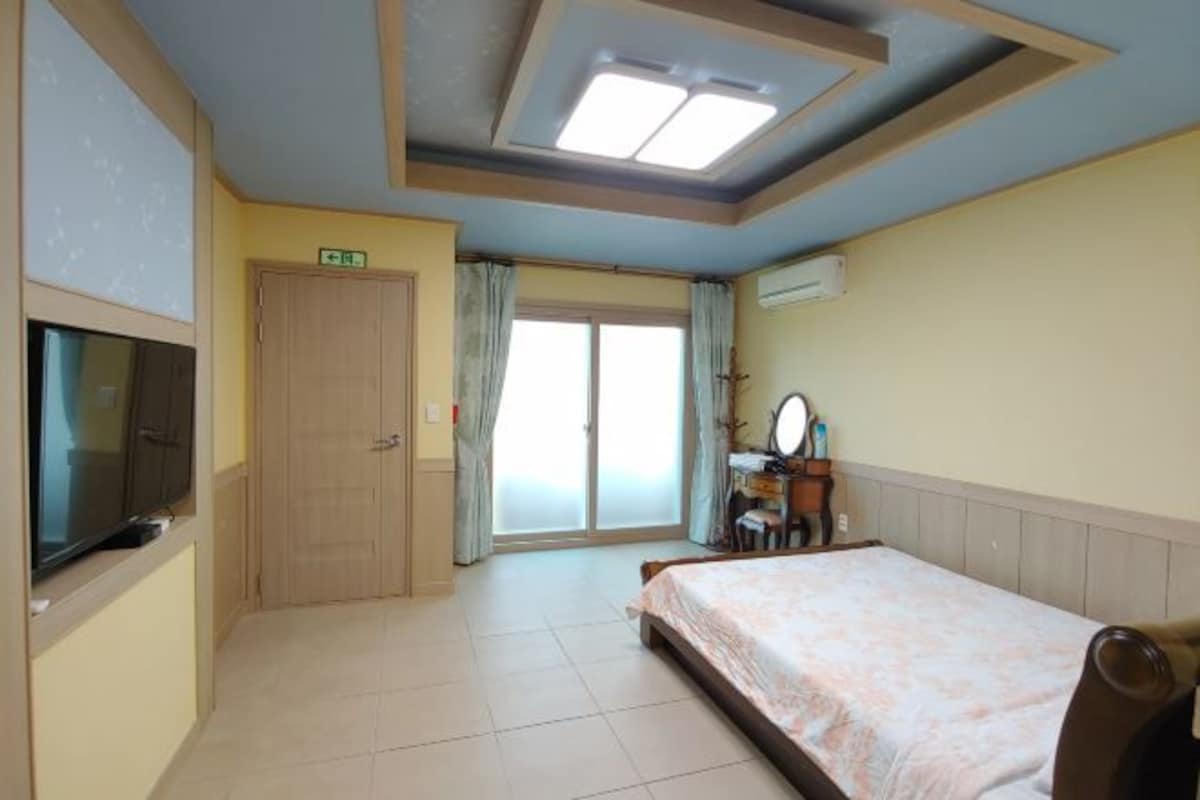 A hotel room with a bed, a television, a desk with a mirror, and a sliding door to the outside.