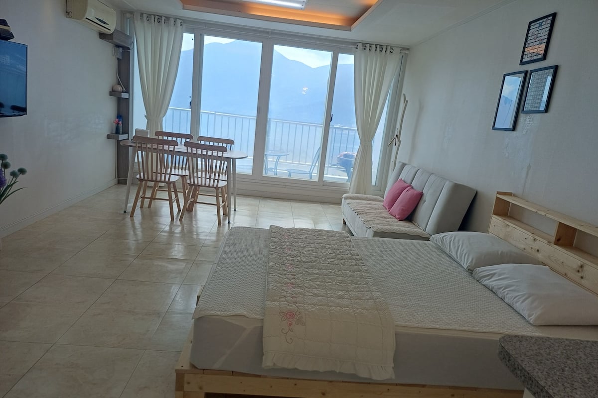 Une chambre à coucher comprenant un lit, un canapé, une table avec des chaises et une vue sur les montagnes, visible à travers de grandes fenêtres.
