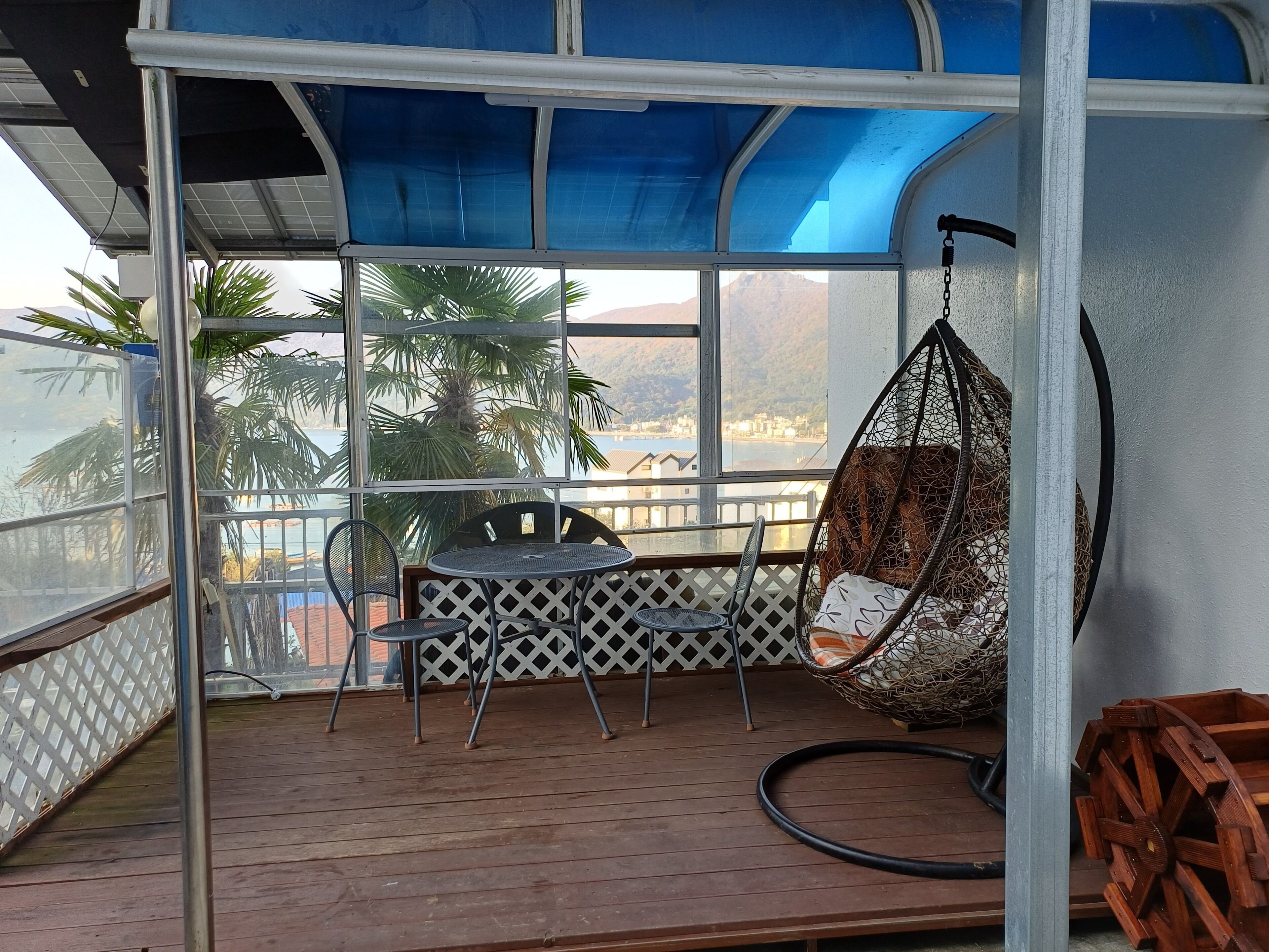 A balcony with a table and chairs, a hanging chair, and a view of the sea and mountains.