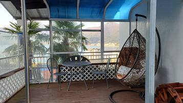 A balcony with a table and chairs, a hanging chair, and a view of the sea and mountains.