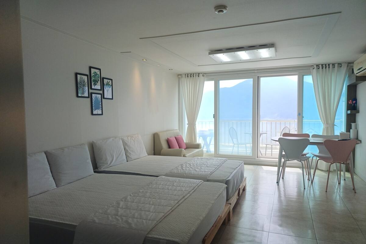 Une chambre d’hôtel avec deux lits, un balcon avec une table et des chaises, et une vue sur la mer.