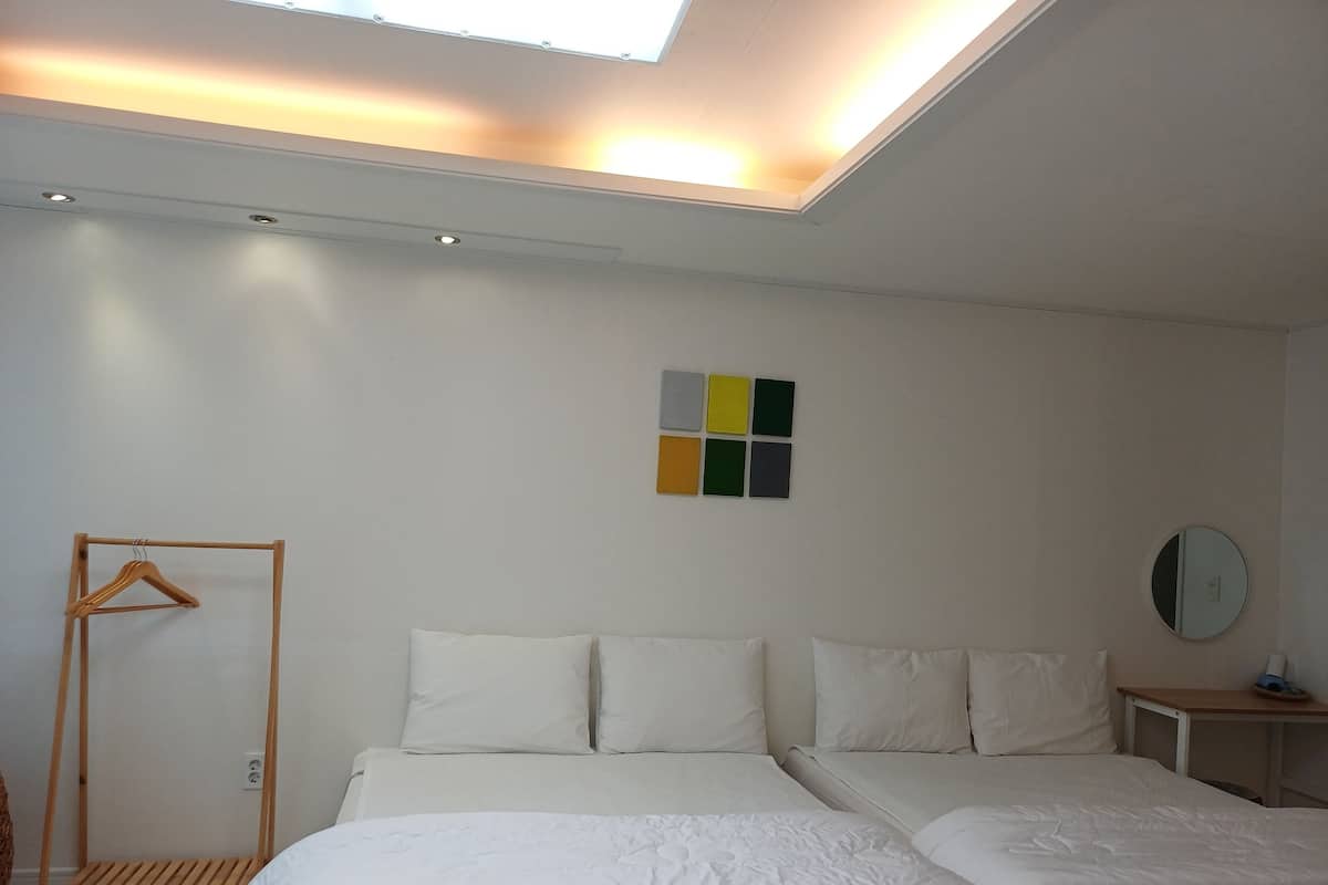 Une chambre d’hôtel avec un lit, un cintre en bois, une petite table, un miroir et un luminaire au plafond.