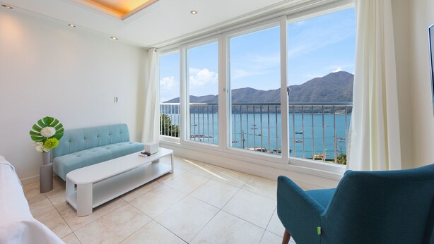 A modern living room with a sofa, a coffee table, and a view of the sea and mountains. - Melodia Pension (Geoje)