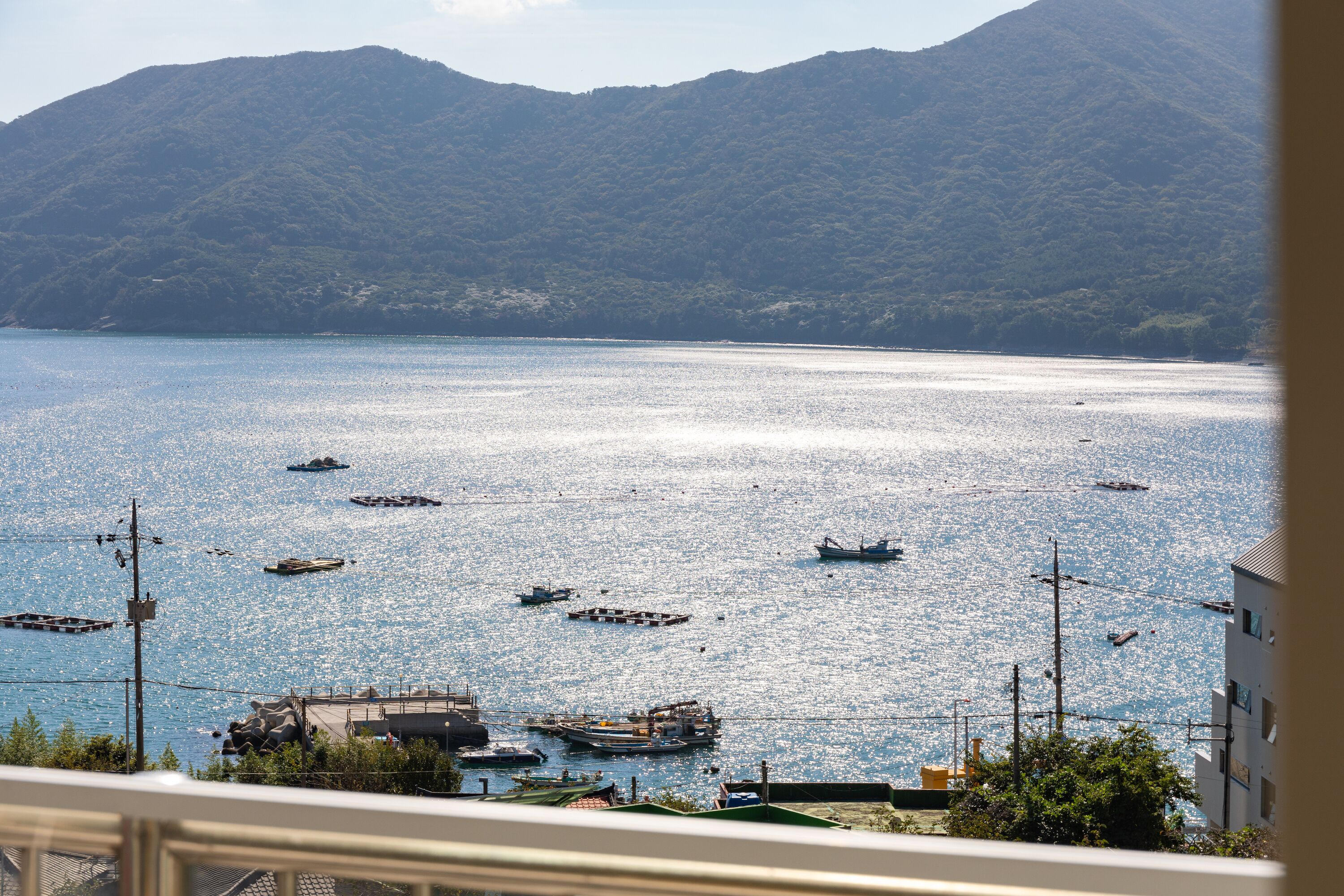 Vista costeira com barcos na água e montanhas ao fundo.