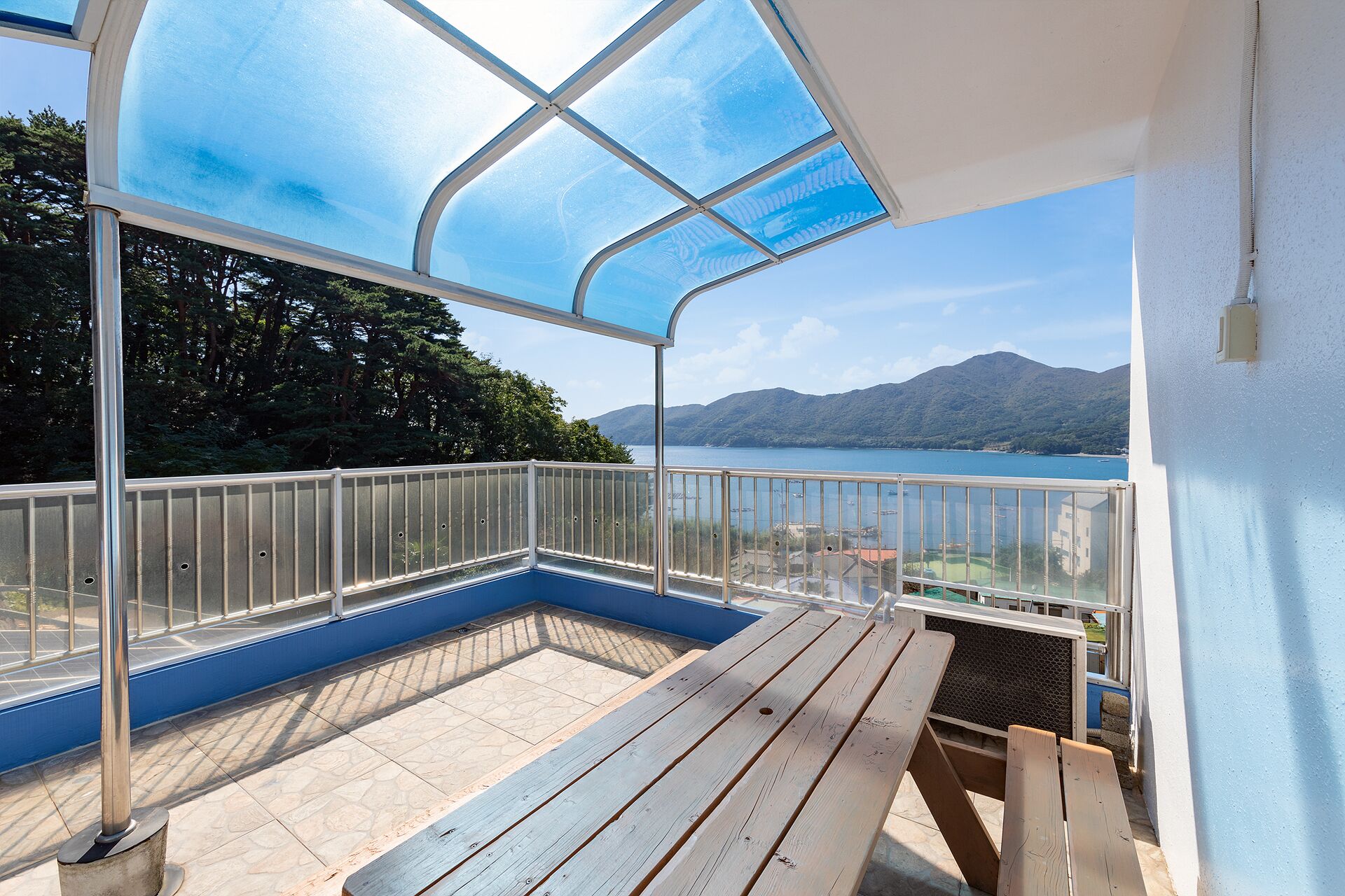 A balcony with a view of a lake and mountains, a wooden bench, and a glass enclosure.