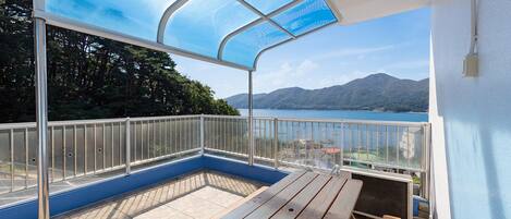 A balcony with a view of a lake and mountains, a wooden bench, and a glass enclosure.