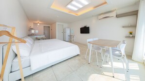 A modern bedroom with a large bed, a dining table with chairs, a ceiling light, and a small kitchen area in the background. - Melodia Pension (Geoje)