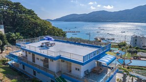 A multi-story building with a rooftop terrace overlooking a body of water and mountains. - Melodia Pension (Geoje)