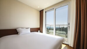 Una habitación de hotel con una cama grande, vistas a través de un ventanal corredero y piso de madera.
