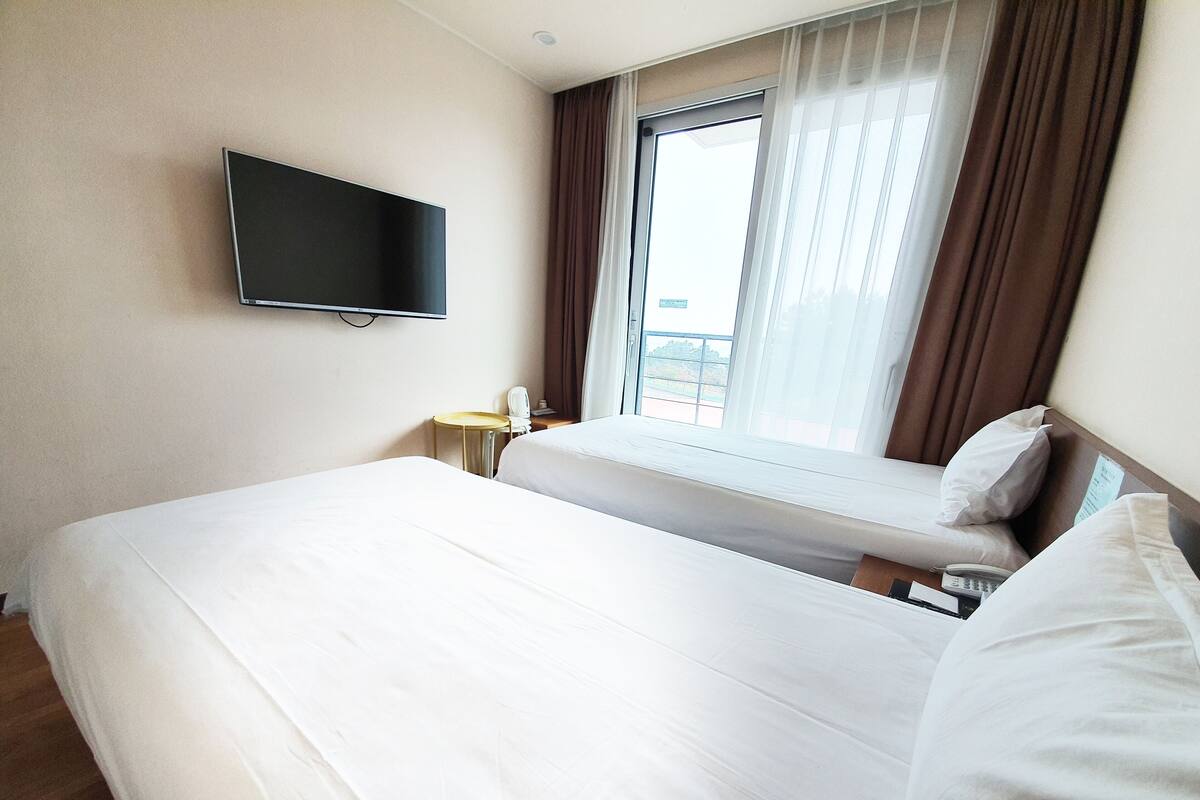 Quarto de hotel com cama, televisão na parede, mesa de cabeceira e janela com cortinas.