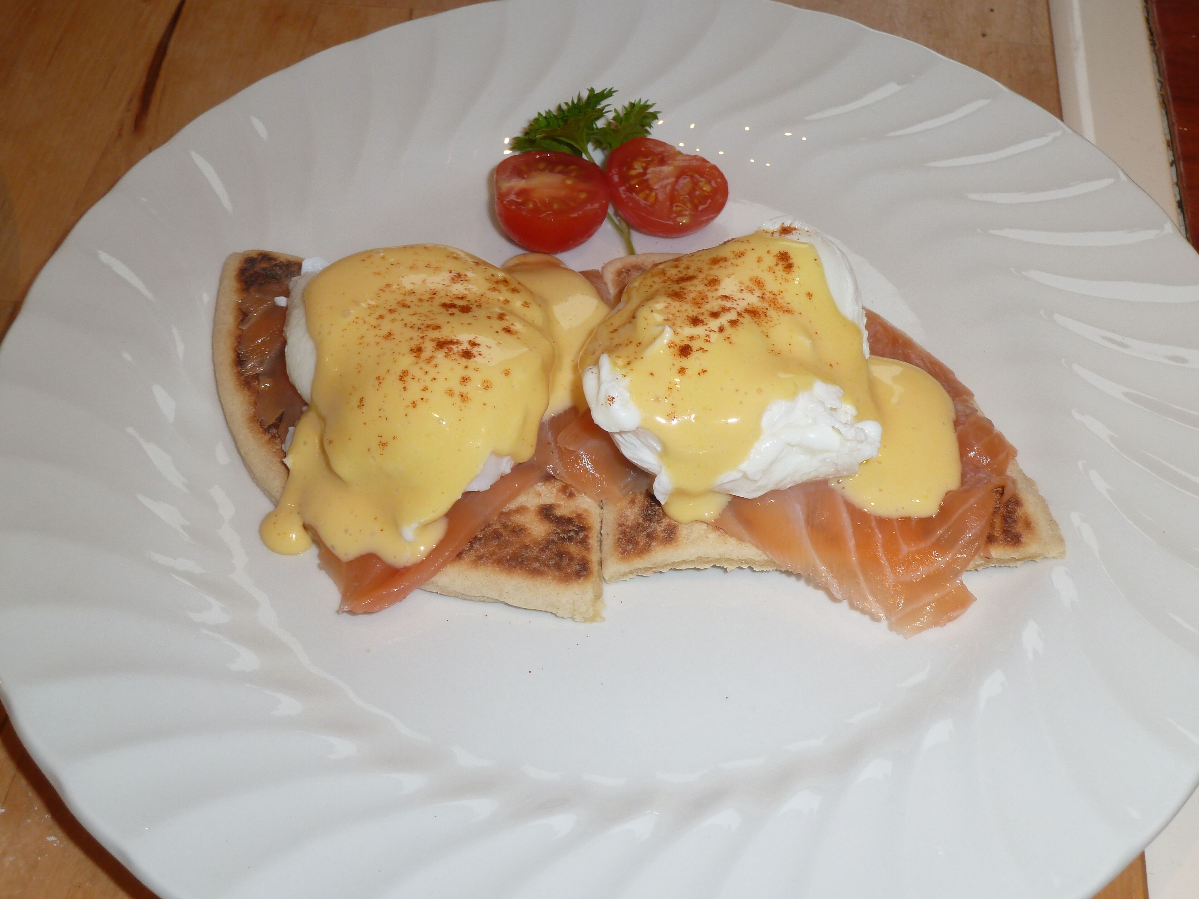 A plate with eggs benedict, smoked salmon, and cherry tomatoes.