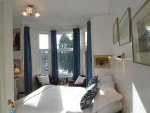 Habitación de hotel con una cama grande, un escritorio con lámpara, una silla y vista al exterior a través de una ventana con cortinas.