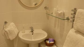 A bathroom with a sink, mirror, towel rack, glass shelf, and a small cabinet.