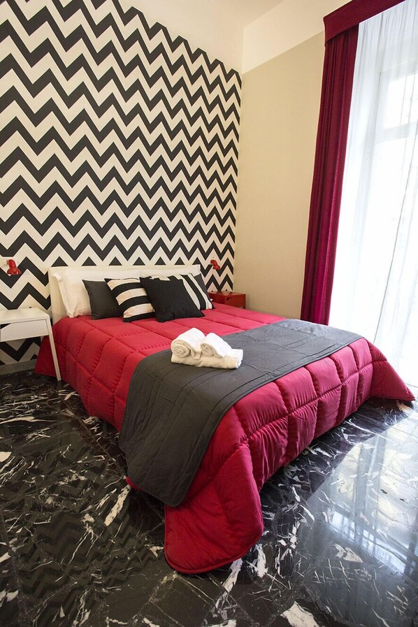 Une chambre d’hôtel avec un lit, une table de chevet, un mur orné d’un motif en chevrons rouge et noir, et un sol en marbre.