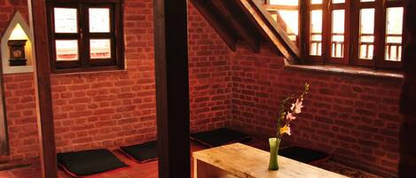 Una habitación con pared de ladrillo, un banco de madera, una pequeña mesa con un jarrón y una ventana con vistas.