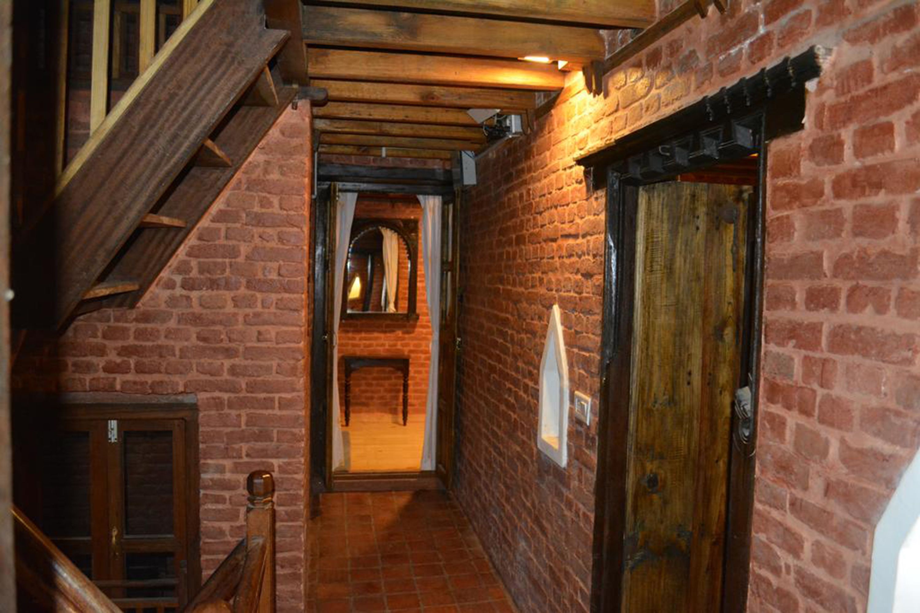A narrow brick corridor with wooden beams and a wooden door.