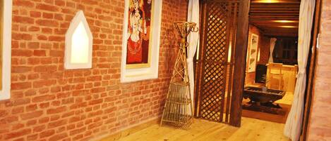 Una habitación rústica con pared de ladrillo, cama de madera, un cuadro enmarco y una puerta tradicional.