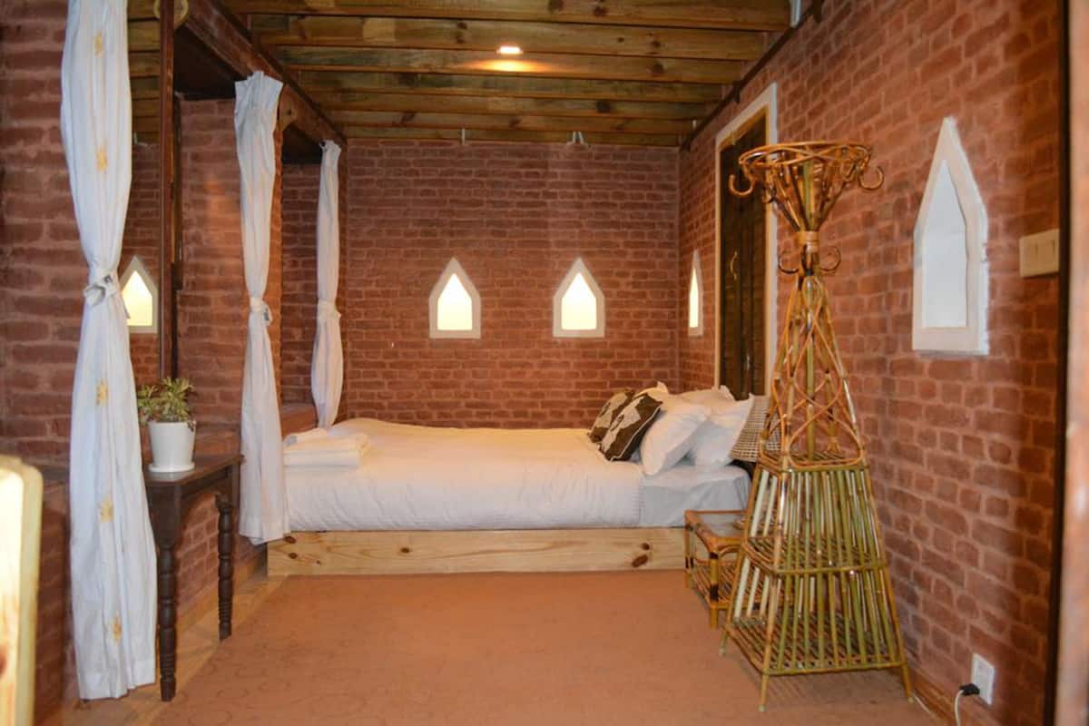 A rustic bedroom with a brick wall, a wooden bed, a canopy bed, and a small table with a plant.