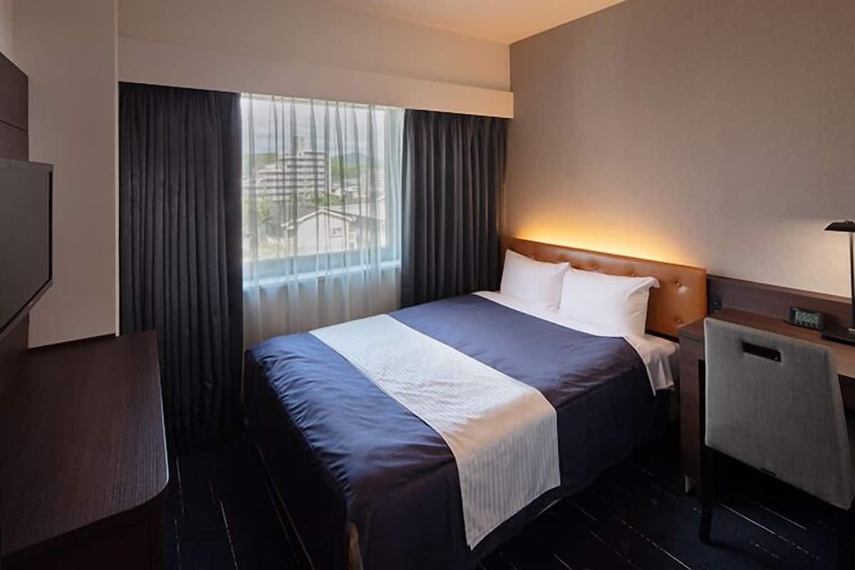 A hotel room with a large bed, a desk, a chair, and a TV.