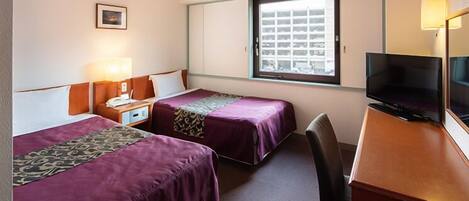 Habitación de hotel con dos camas, un escritorio, televisor y ventana con vistas a edificios.