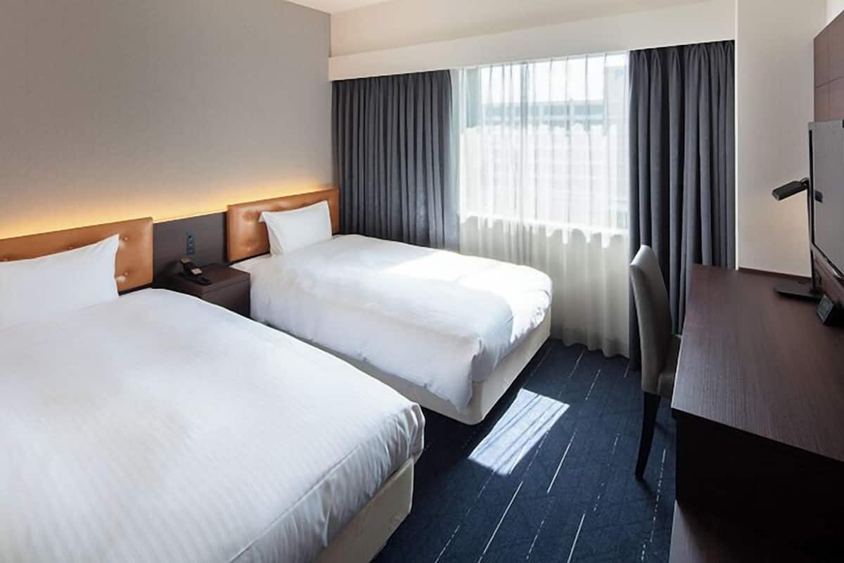 A hotel room with two beds, a desk, and a TV.