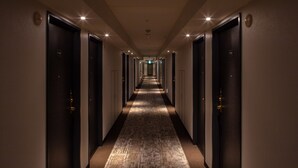 A hotel hallway with multiple doors, each marked with a number. The hallway is well-lit with ceiling lights and features a patterned carpet. - Shin Iizuka Station Hotel (Iizuka)
