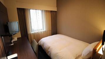 Habitación de hotel con cama, escritorio con ordenador, televisor y ventana con cortinas.