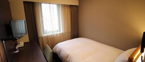 A hotel room with a bed, a desk with a computer, a TV, and a window with curtains.