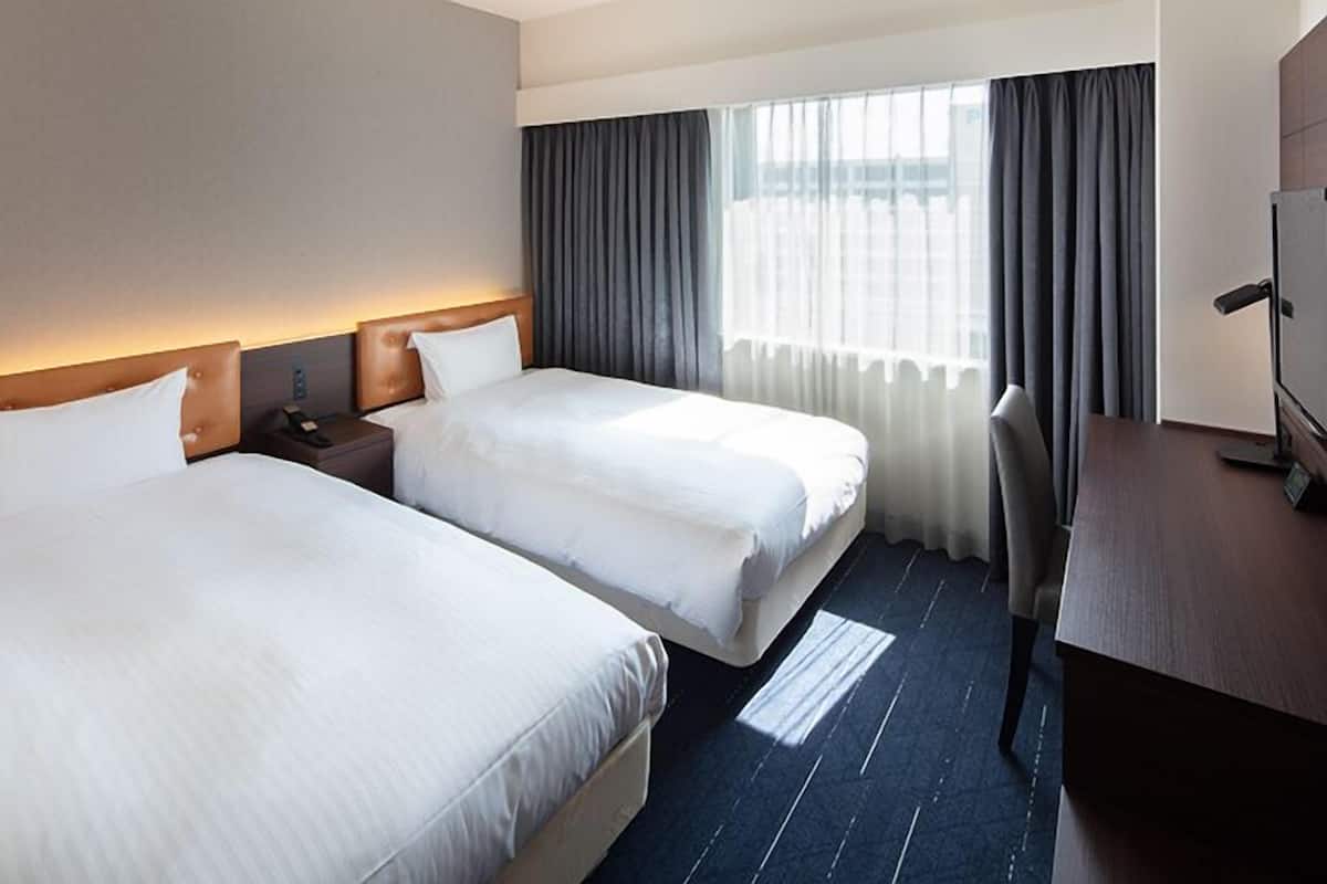 A hotel room with two beds, a desk, and a TV.