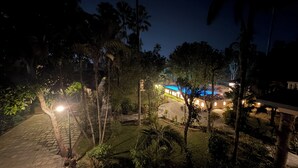 Une vue nocturne d’un complexe hôtelier avec une piscine, des palmiers et un sentier en pierre.