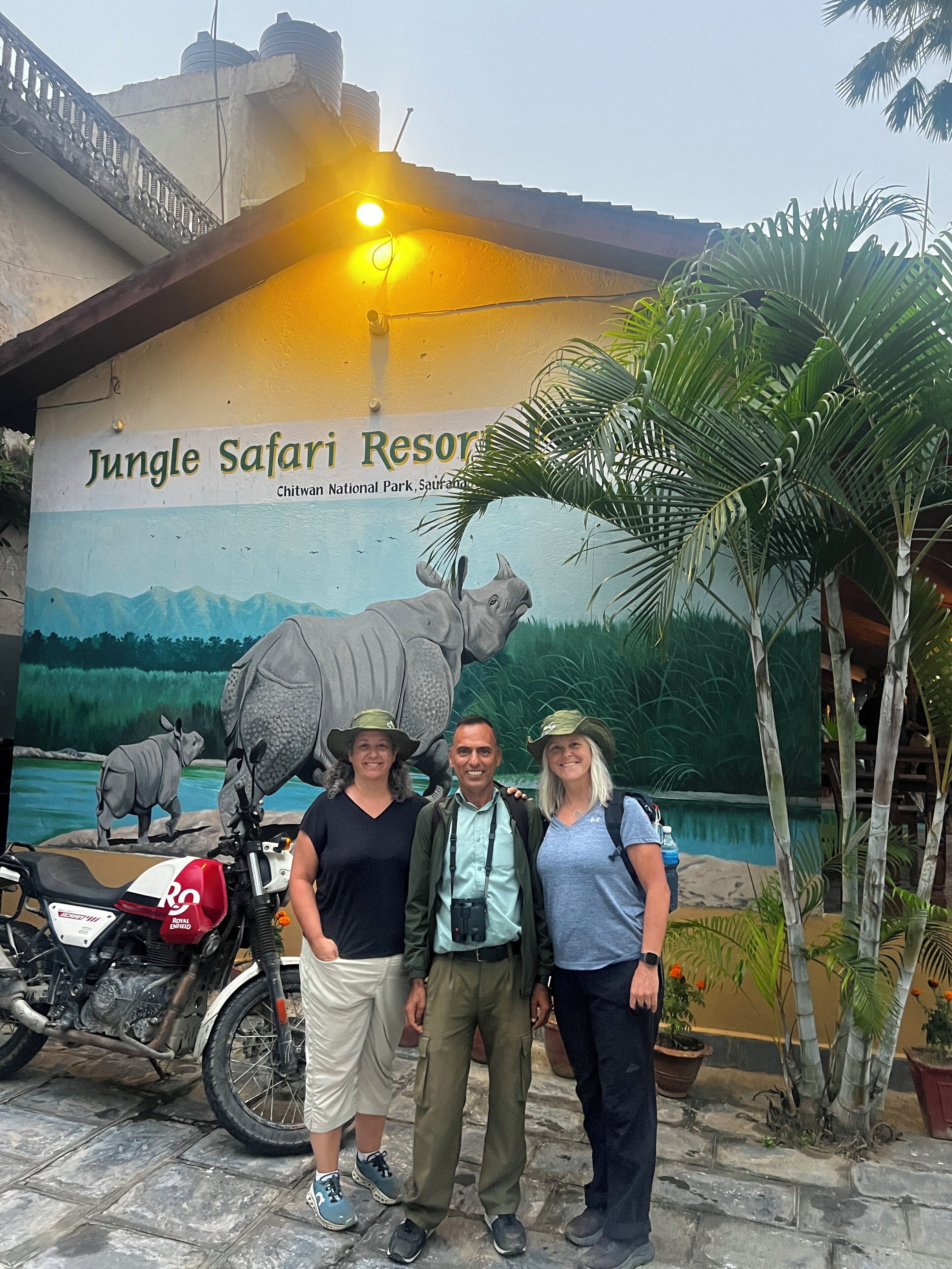 A sign for Jungle Safari Resort with a mural of a rhinoceros and elephants, a motorcycle, and a few people standing in front.