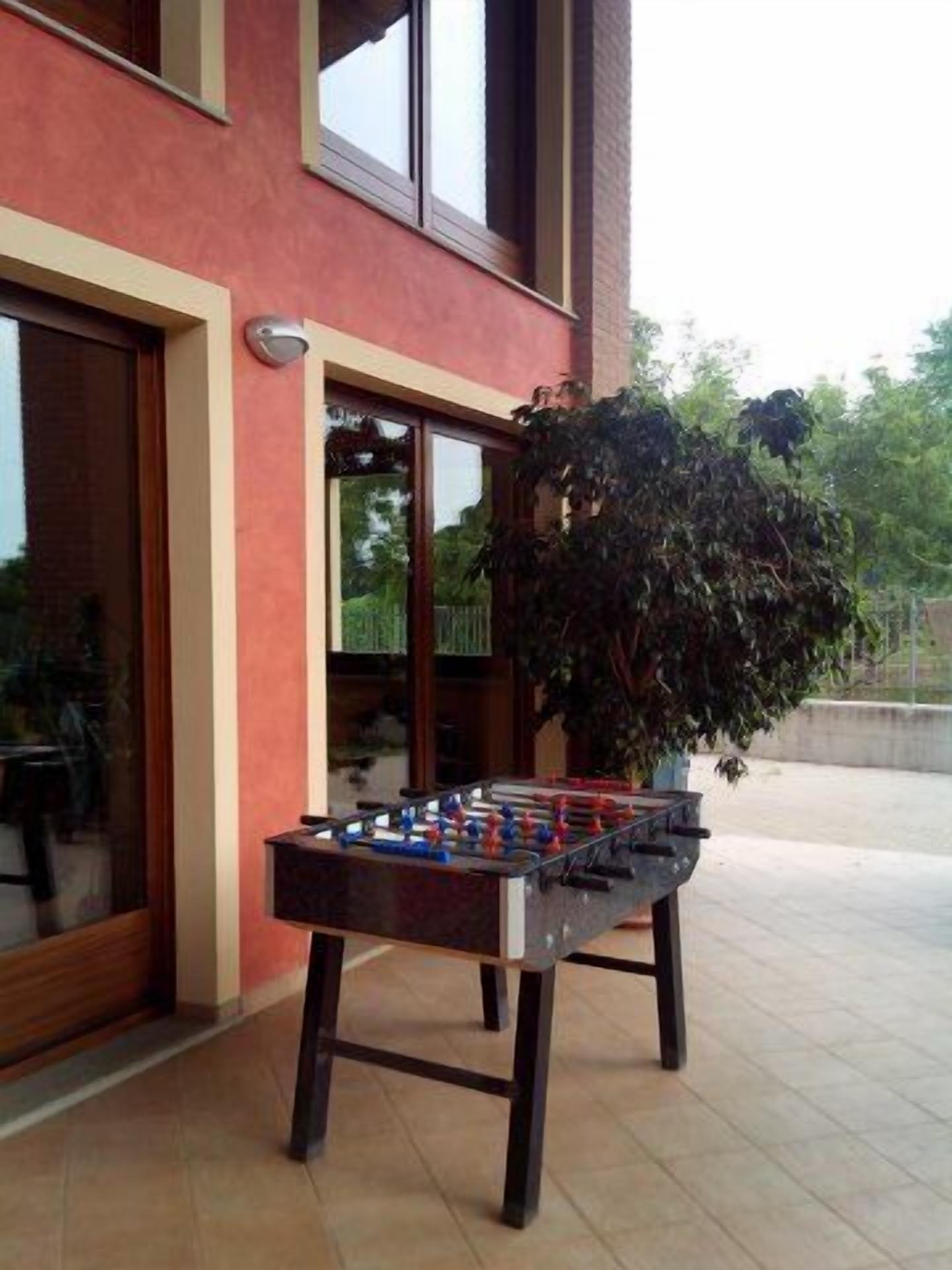 Una mesa de fútbol de mesa al aire libre frente a un edificio con ventanas amplias y una planta en maceta cerca.