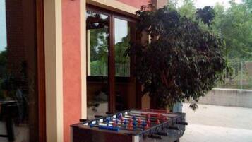 Una mesa de fútbol de mesa al aire libre frente a un edificio con ventanas amplias y una planta en maceta cerca.