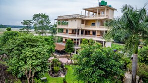 Um edifício com várias andares e varandas, rodeado por vegetação exuberante e um pequeno jardim.