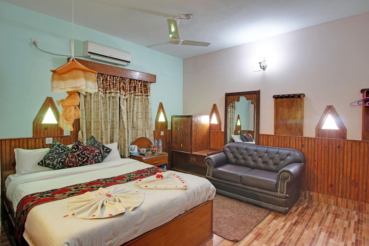 A hotel room with a bed, a sofa, a mirror, and a ceiling fan.