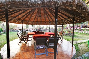 A covered outdoor seating area with tables and chairs, surrounded by a garden with potted plants and flowers. - Hotel Riverside (Sauraha)